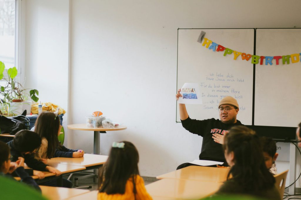 1st grade male teacher showing a paper to a class of students